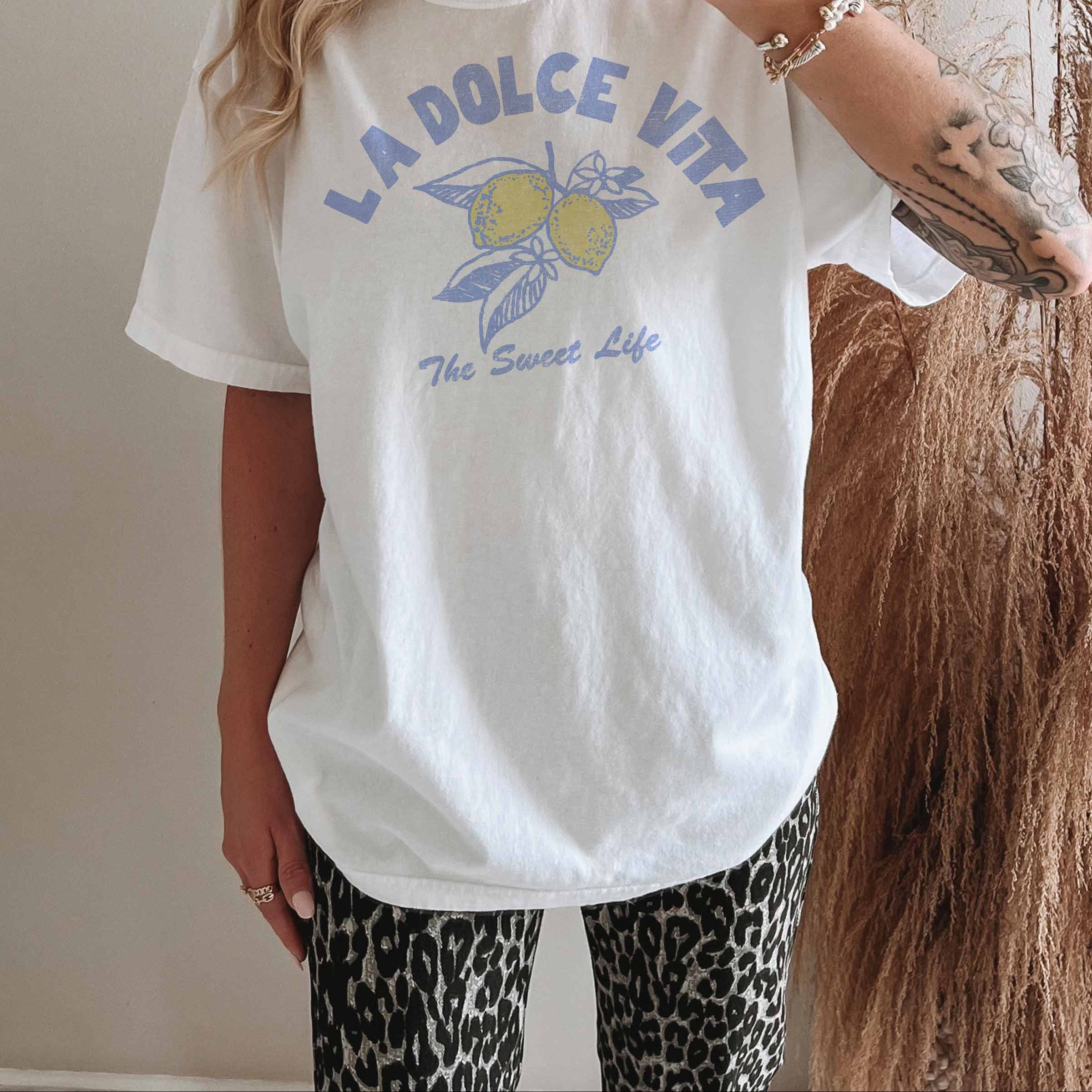 Person trägt ein weißes LA DOLCE VITA T-Shirt mit Grafikprint und lässigem Schnitt.